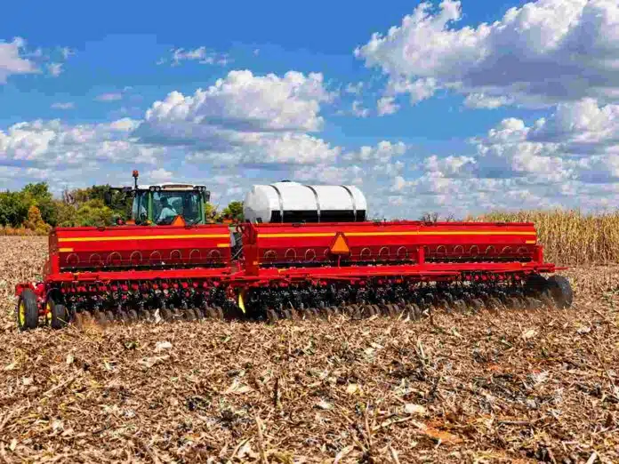 sembradora-girasol-siembra-directa-campo-argentino-ruralnet Sembradora Sunflower de gran porte trabajando sobre rastrojos de maíz en un campo agrícola, bajo un cielo azul con grandes nubes blancas.