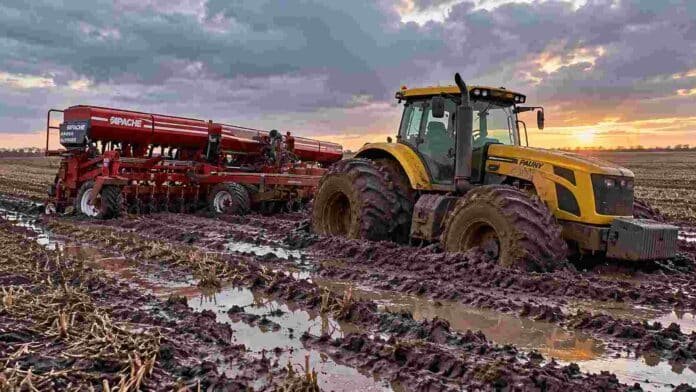Tractor Pauny y sembradora Apache encajados en el barro de un campo en barbecho, con suelo saturado de humedad, huellas profundas y charcos de agua.