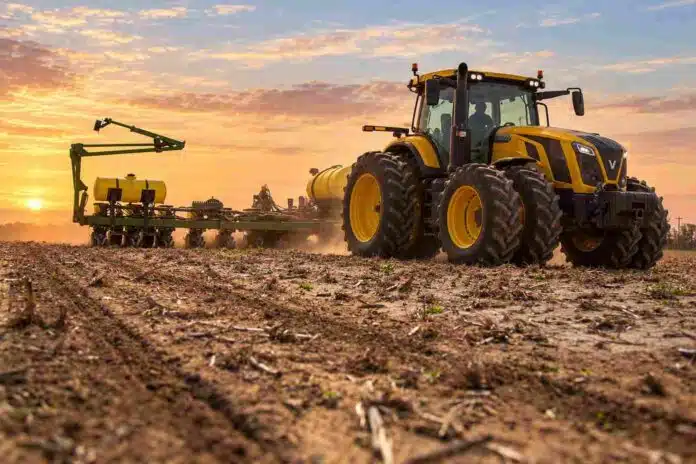 Tractor Valtra amarillo con ruedas duales y sembradora trabajando sobre un lote con rastrojos al amanecer.